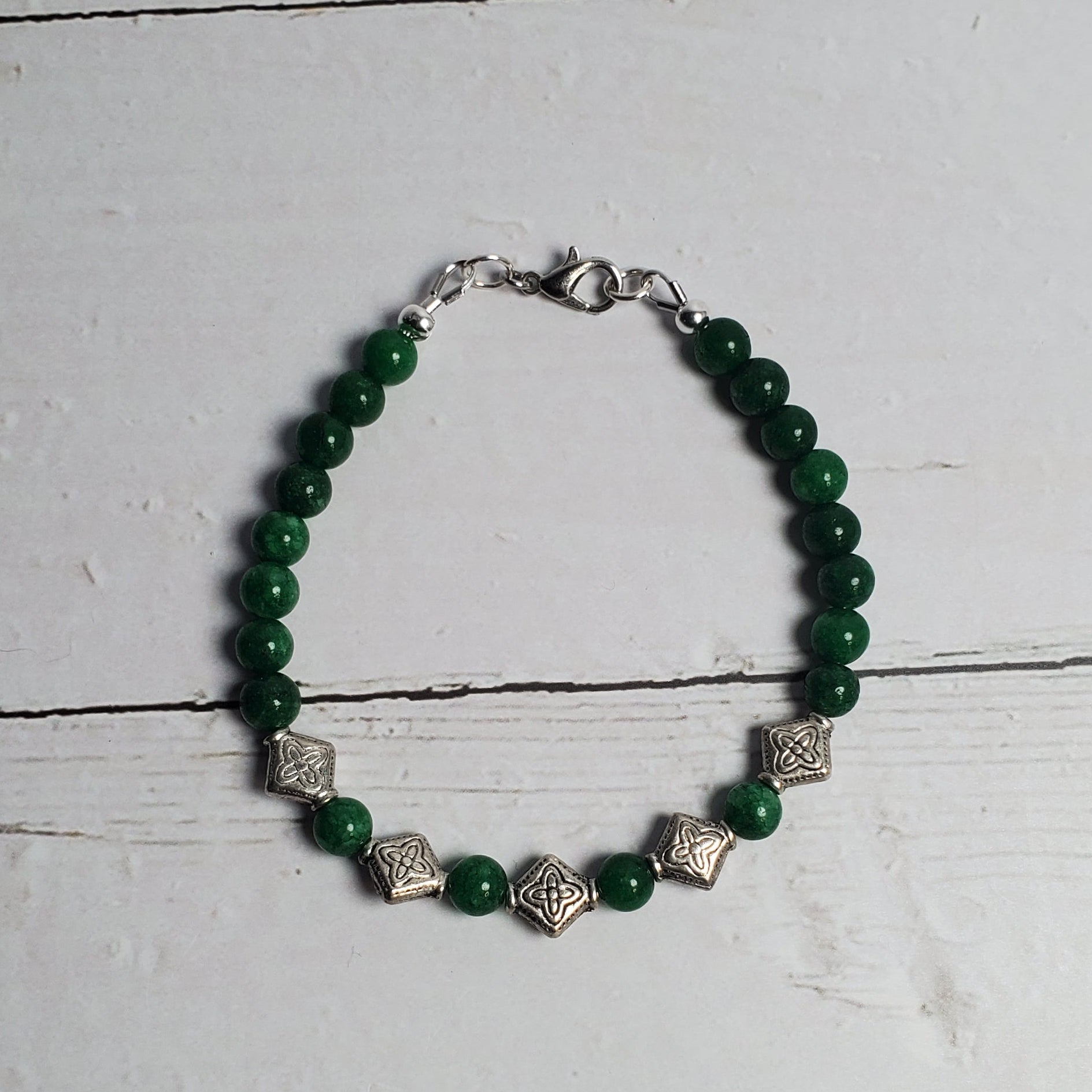 Green beaded bracelet with silver accents on a white wooden surface