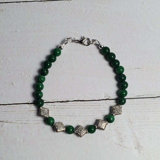 Green beaded bracelet with silver accents on a white wooden surface