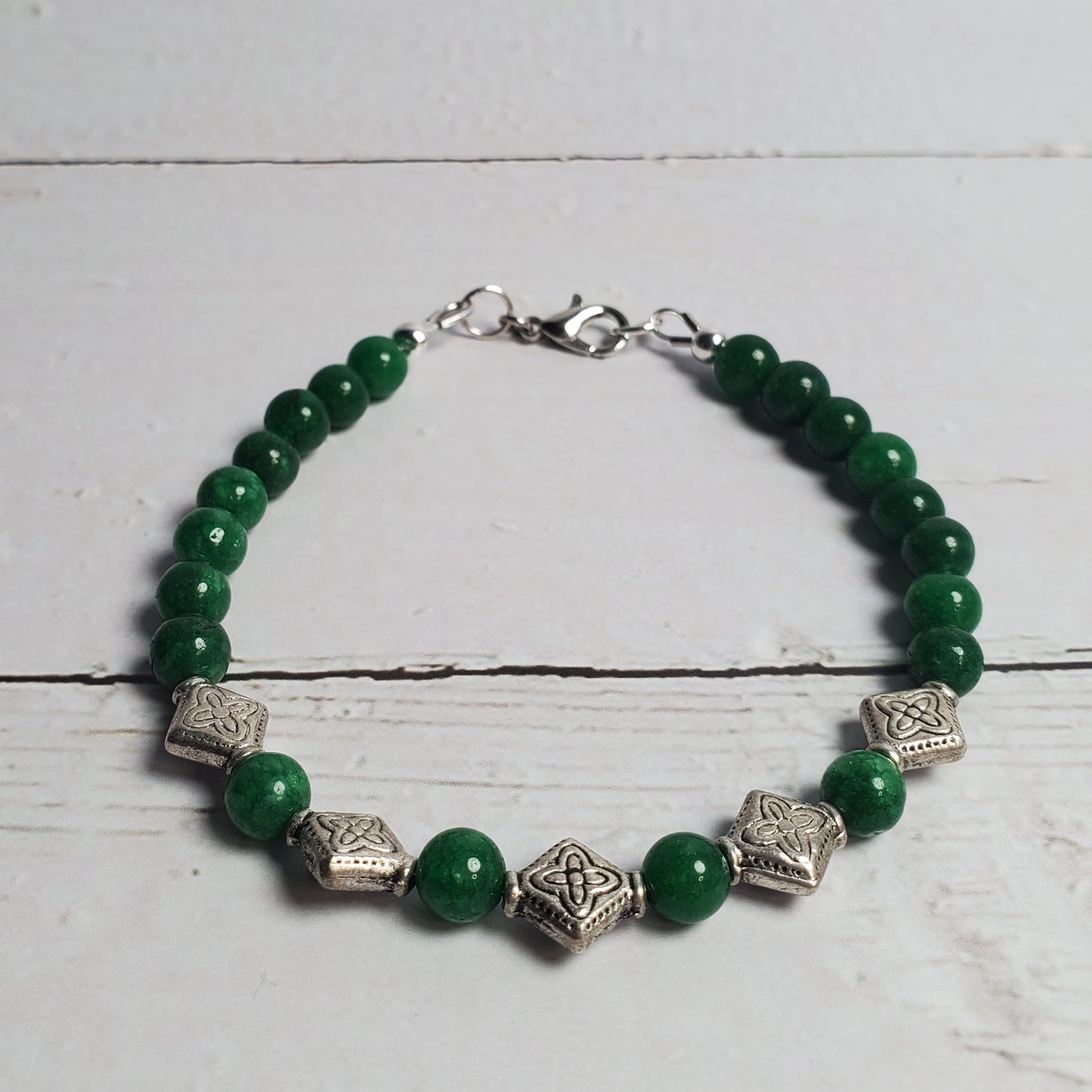 Green beaded bracelet with silver accents on a white wooden surface
