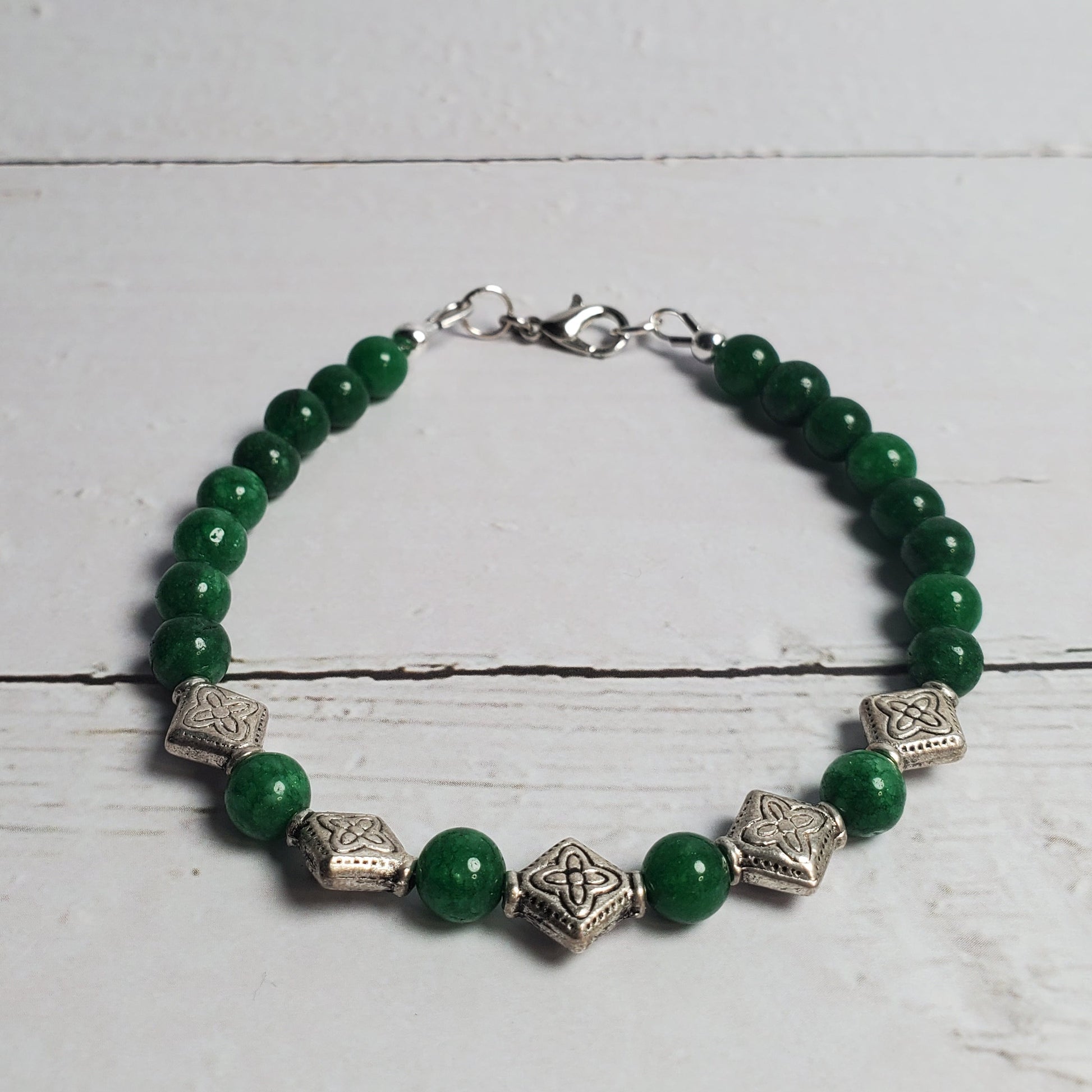Green beaded bracelet with silver accents on a white wooden surface