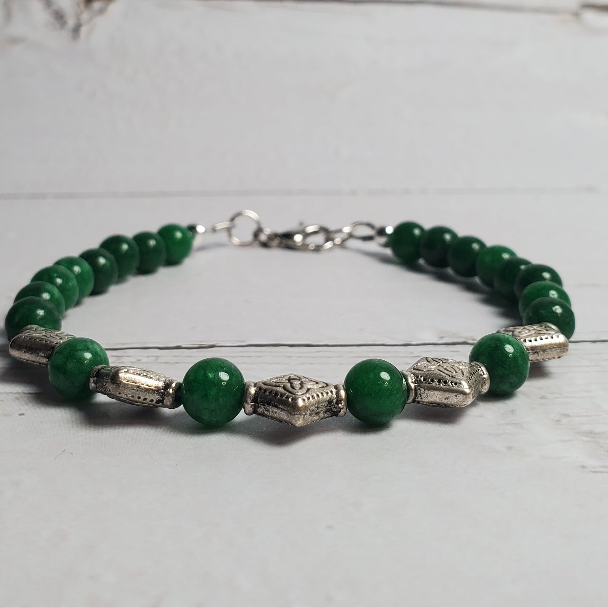 Green beaded bracelet with silver accents on a light wooden surface