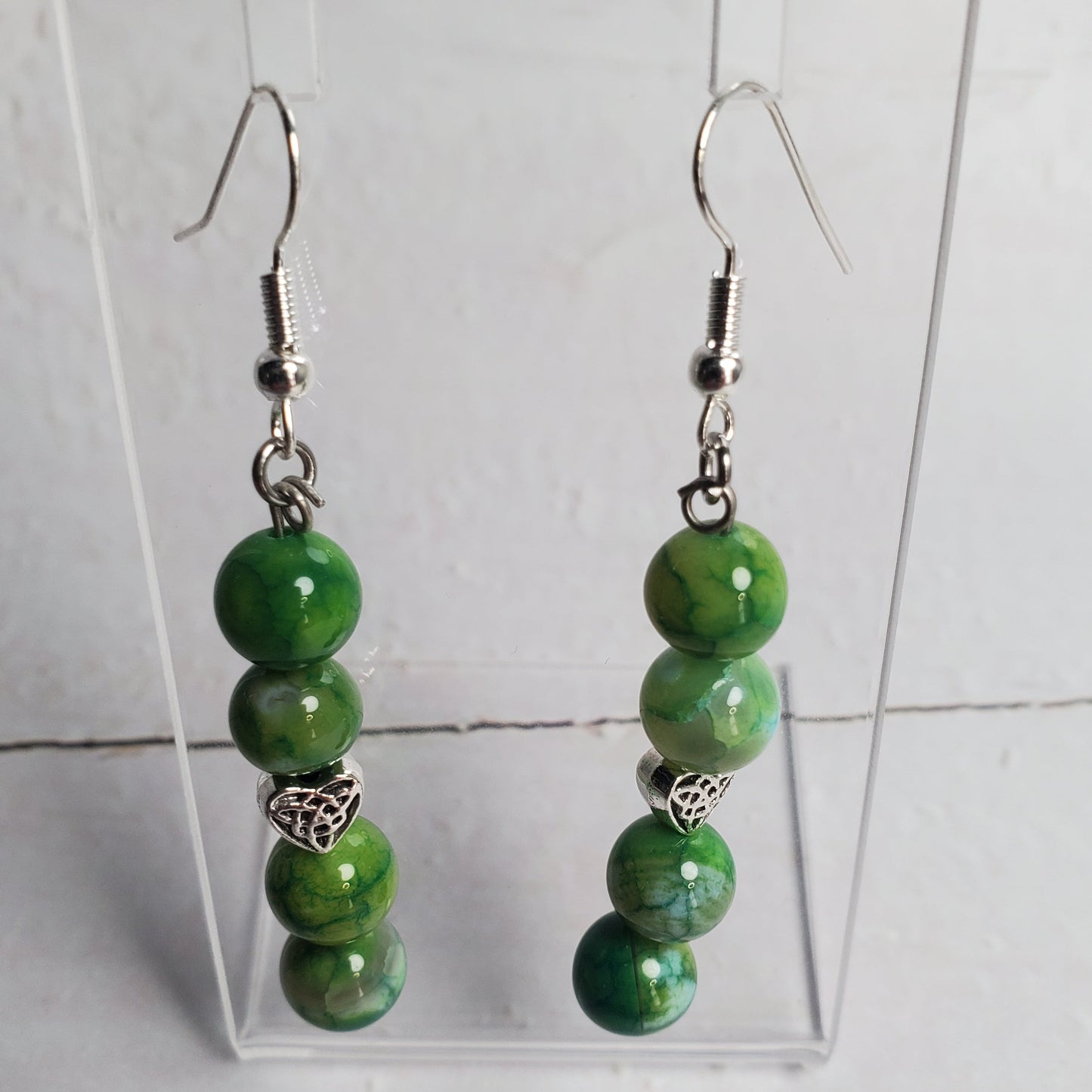 Green beaded earrings on a clear stand against a white background