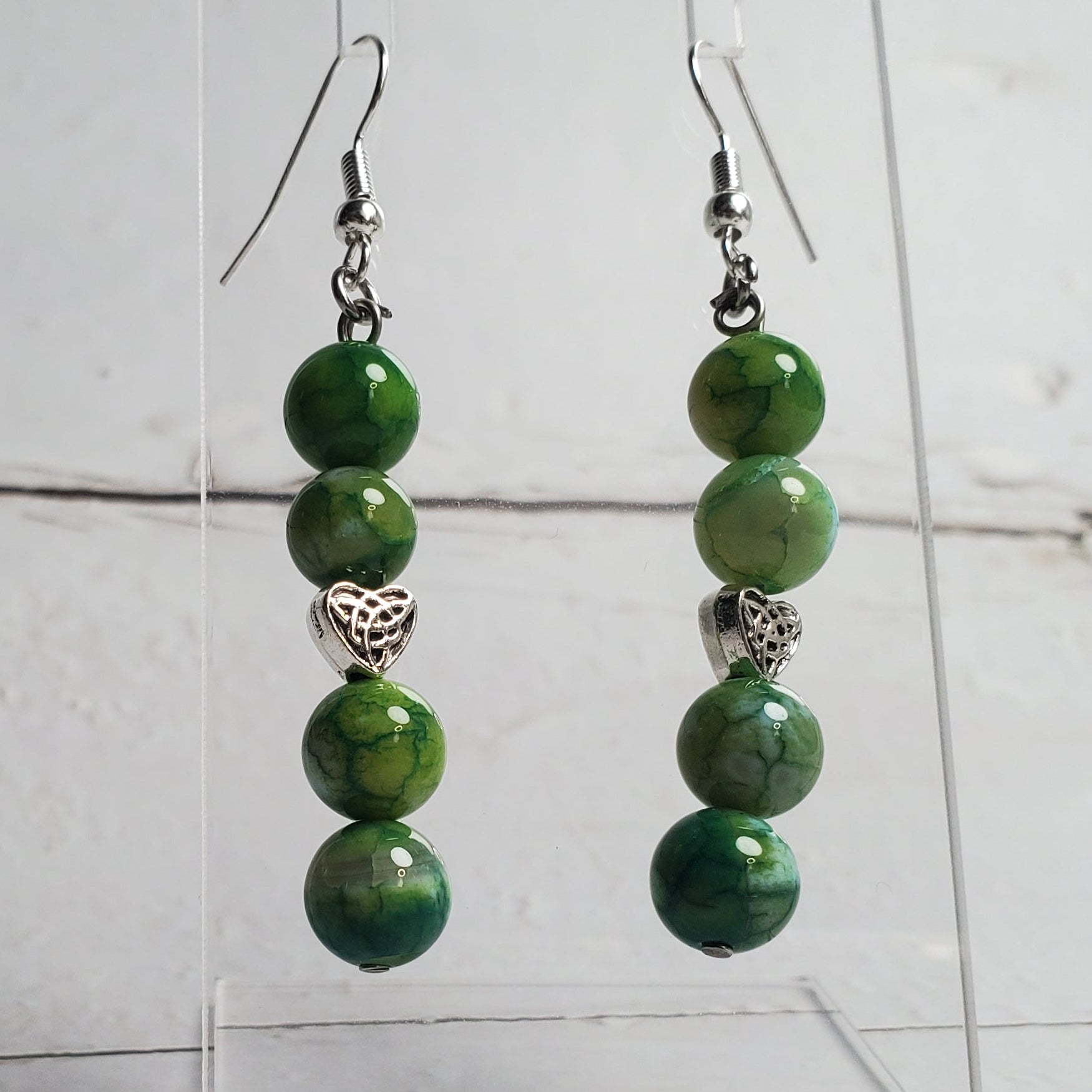 Green beaded earrings on a clear stand against a white wooden background