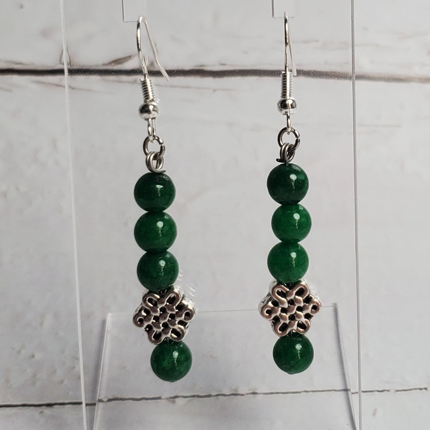 Green beaded earrings on a clear stand against a light wooden background