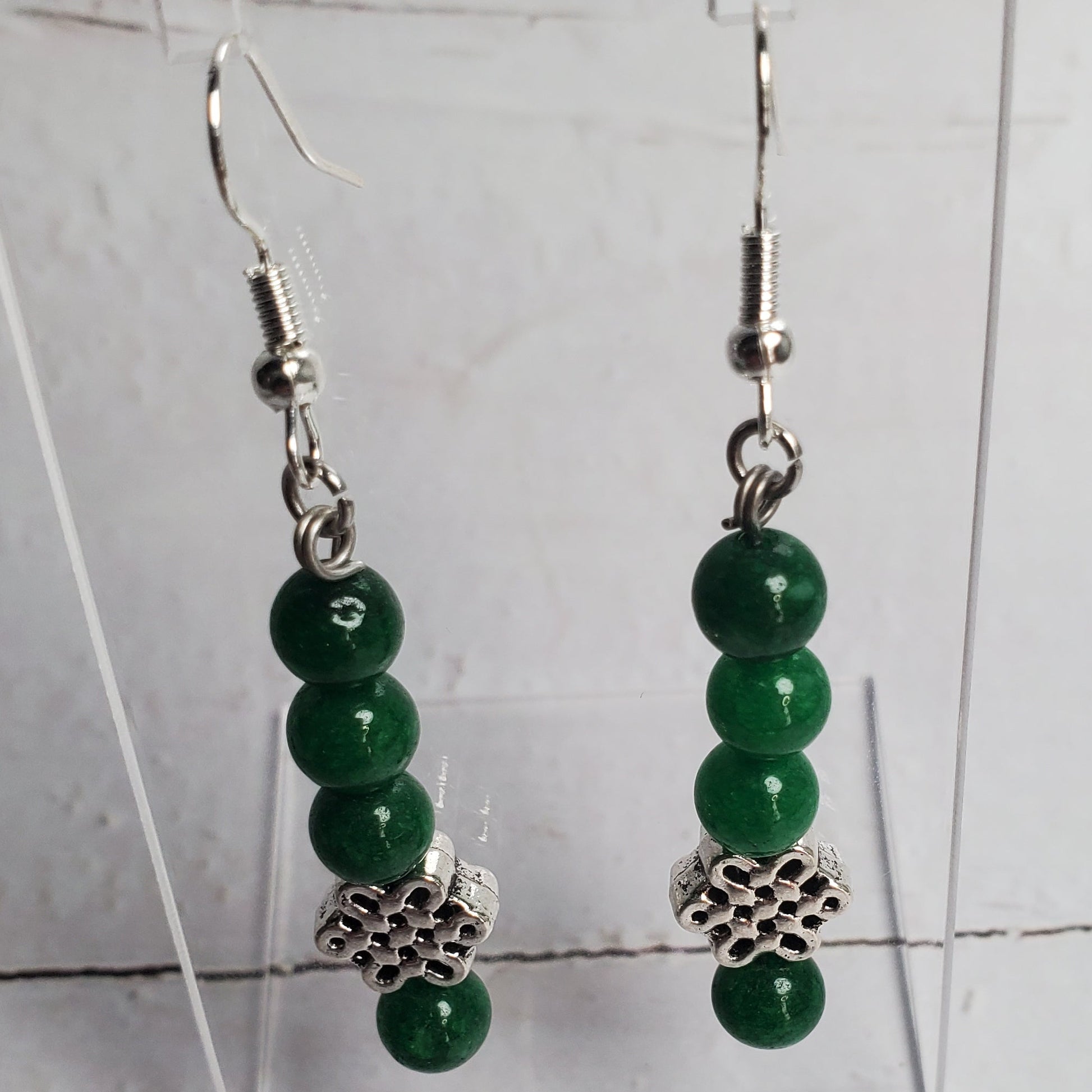 Green beaded earrings on a clear stand against a light gray background