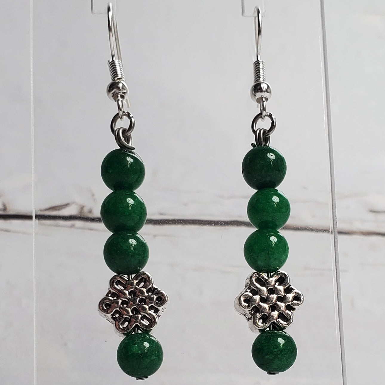 Green beaded earrings on a clear stand against a white wooden background