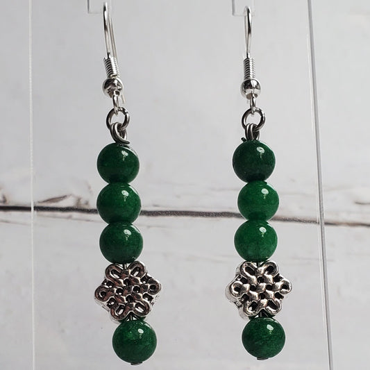 Green beaded earrings on a clear stand against a white wooden background