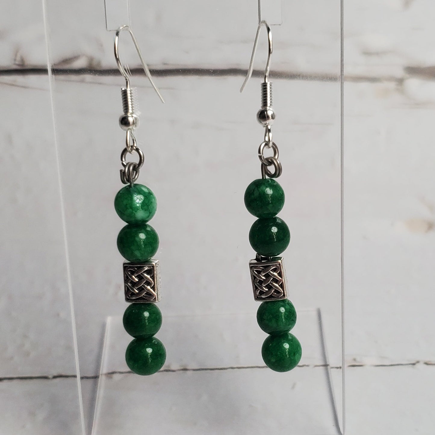 Green beaded earrings on a clear stand against a white wooden background