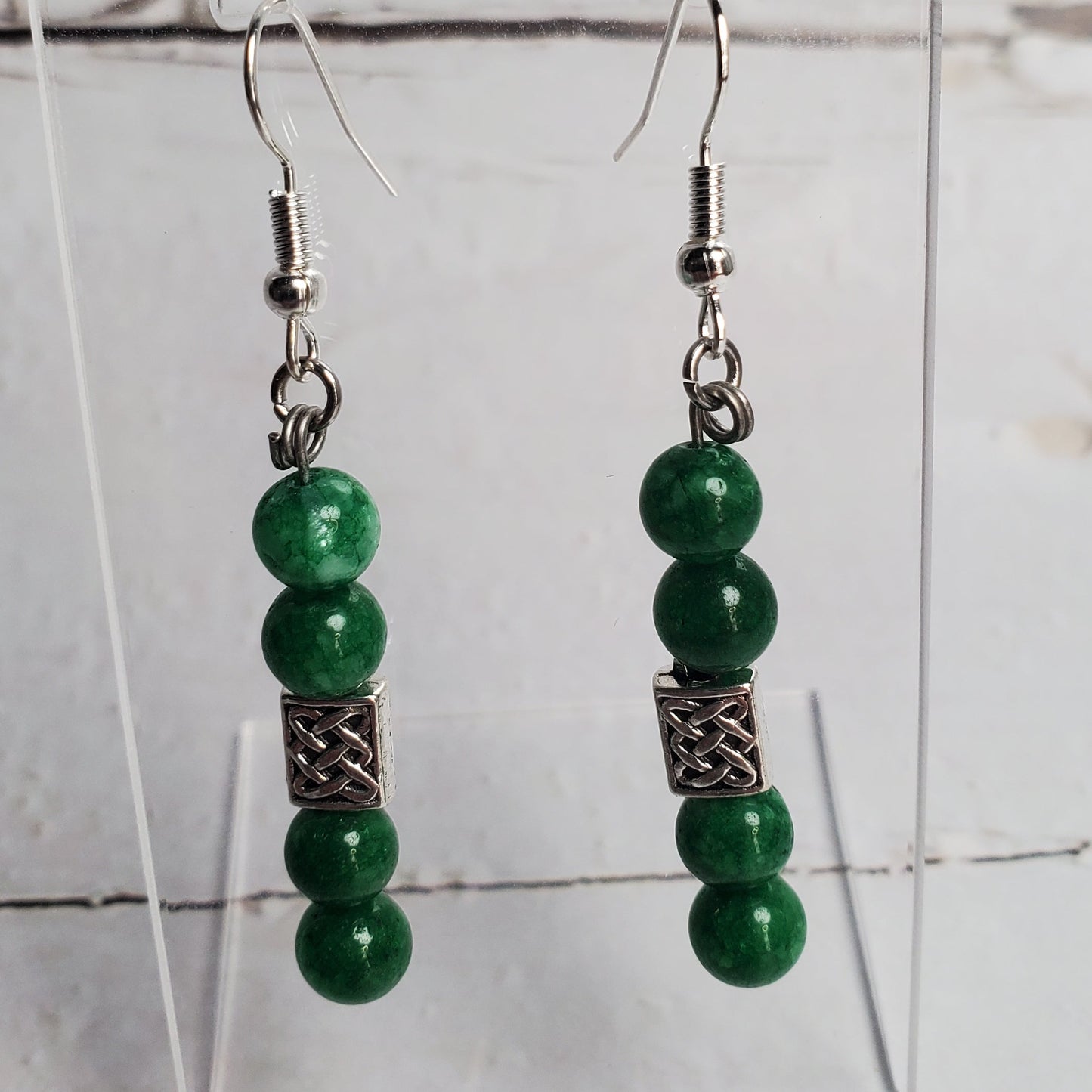 Green beaded earrings on a clear stand against a white background