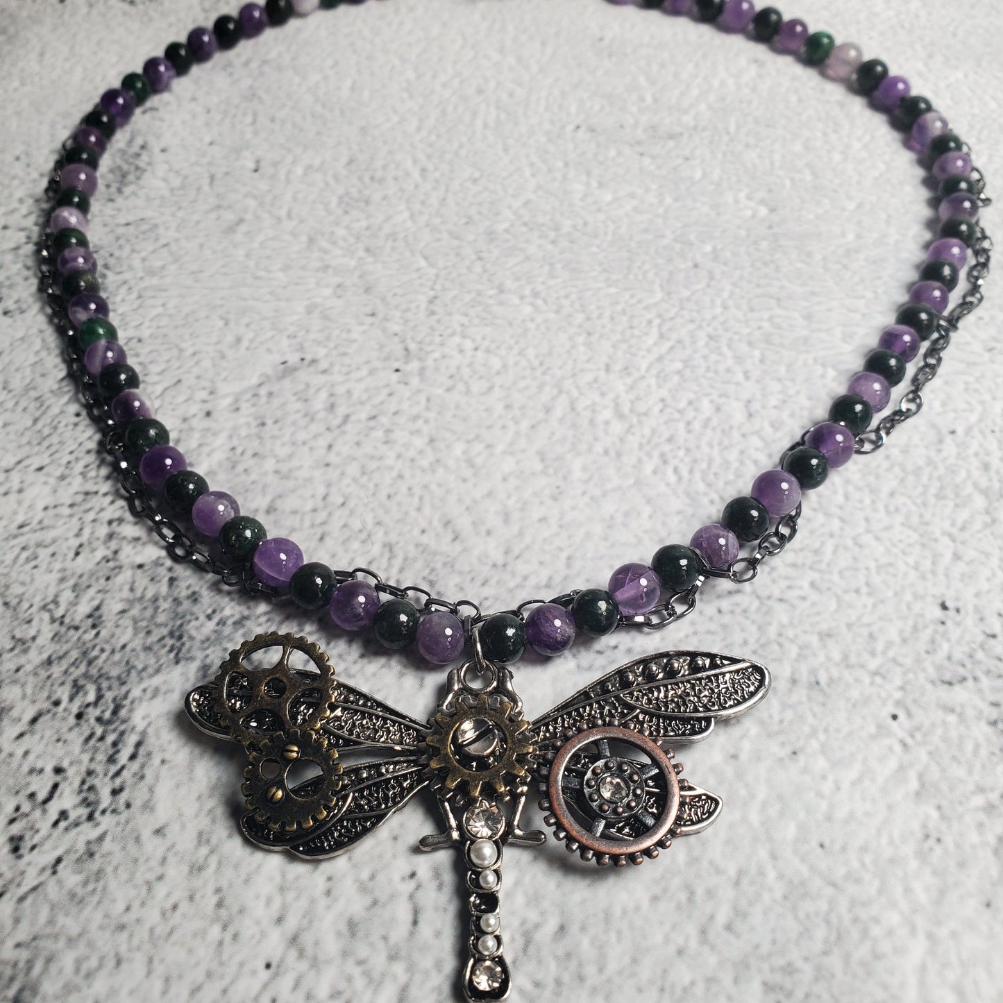 Industrial style necklace with mechanical dragonfly pendant featuring amethyst and emerald gemstones on gunmetal chain