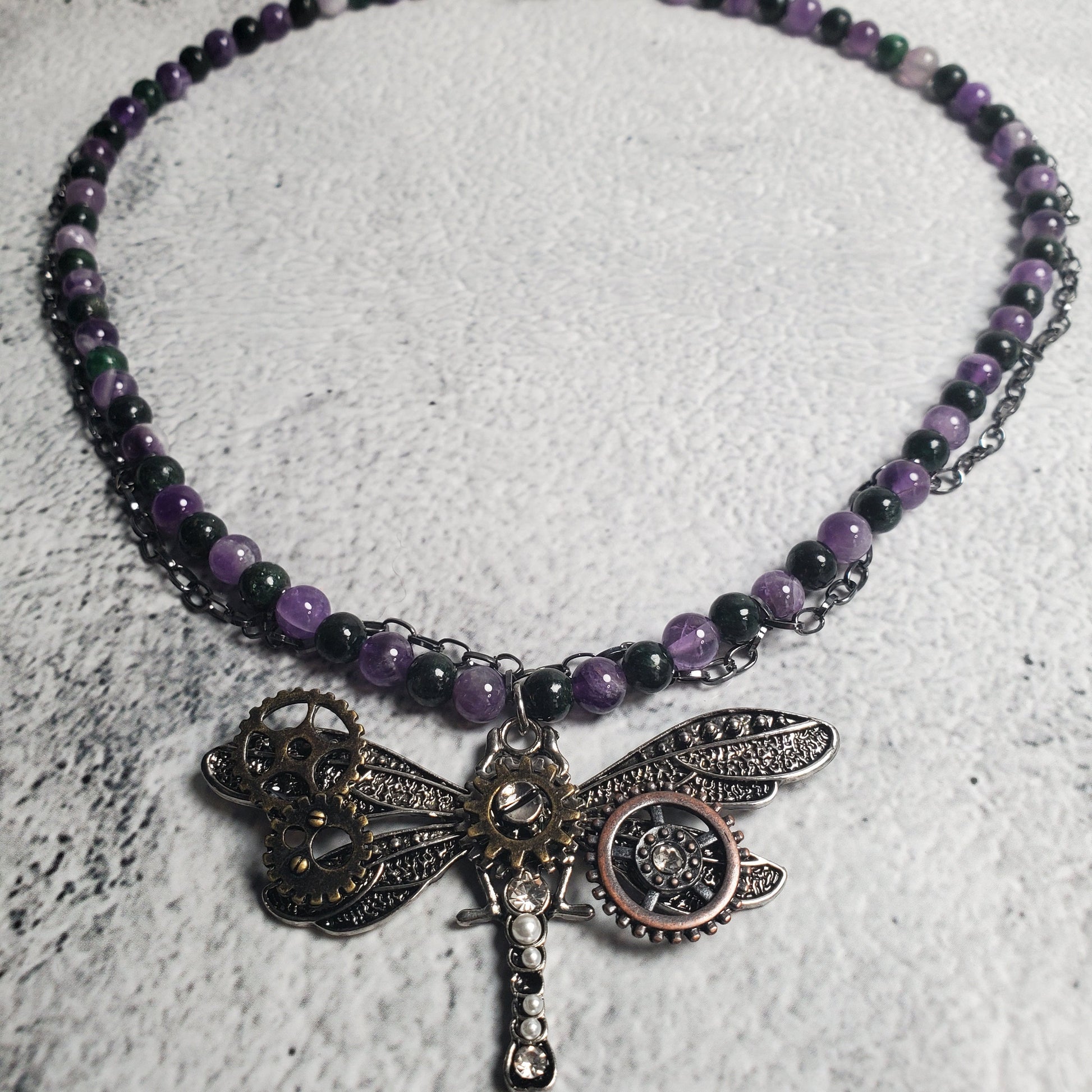 Industrial style necklace with mechanical dragonfly pendant featuring amethyst and emerald gemstones on gunmetal chain