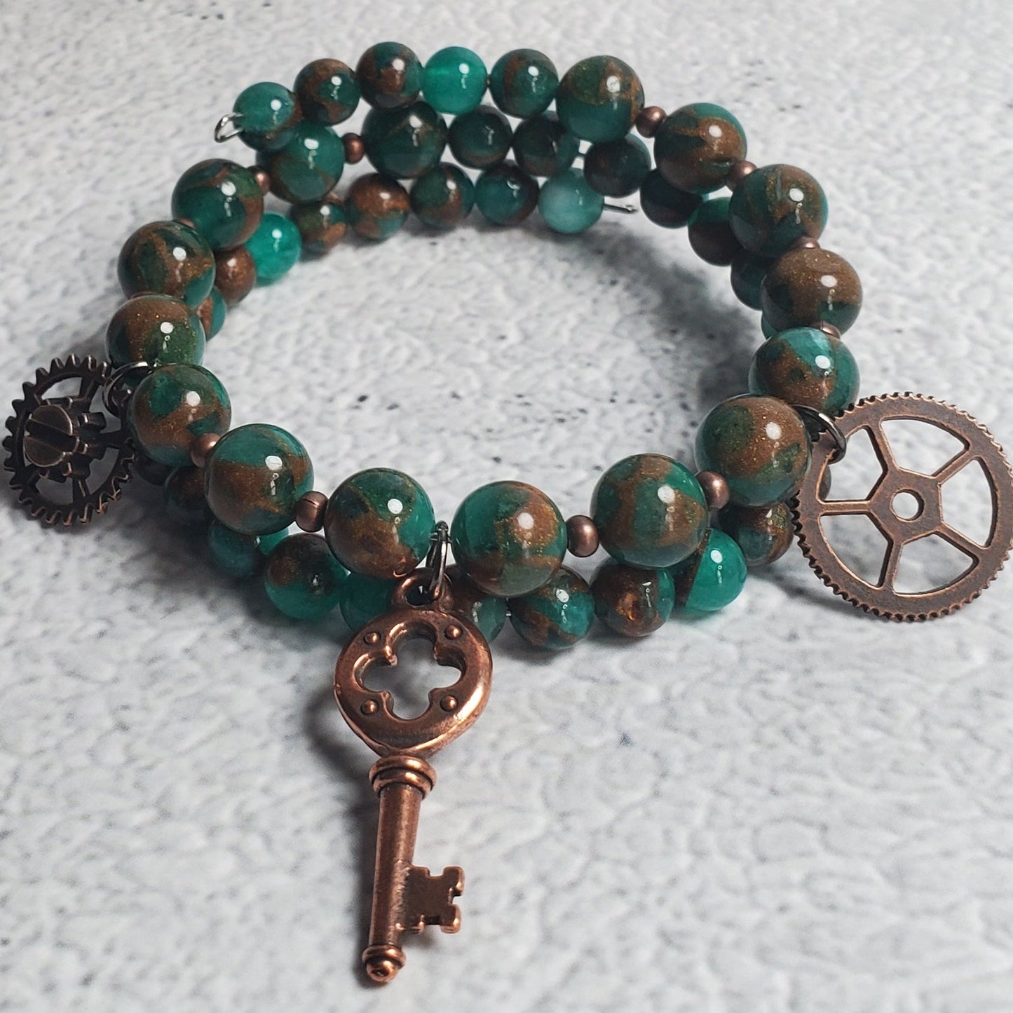 Handcrafted steampunk industrial bracelet with green resin sponge quartz, copper gear, and skeleton key charms on a memory wire cuff