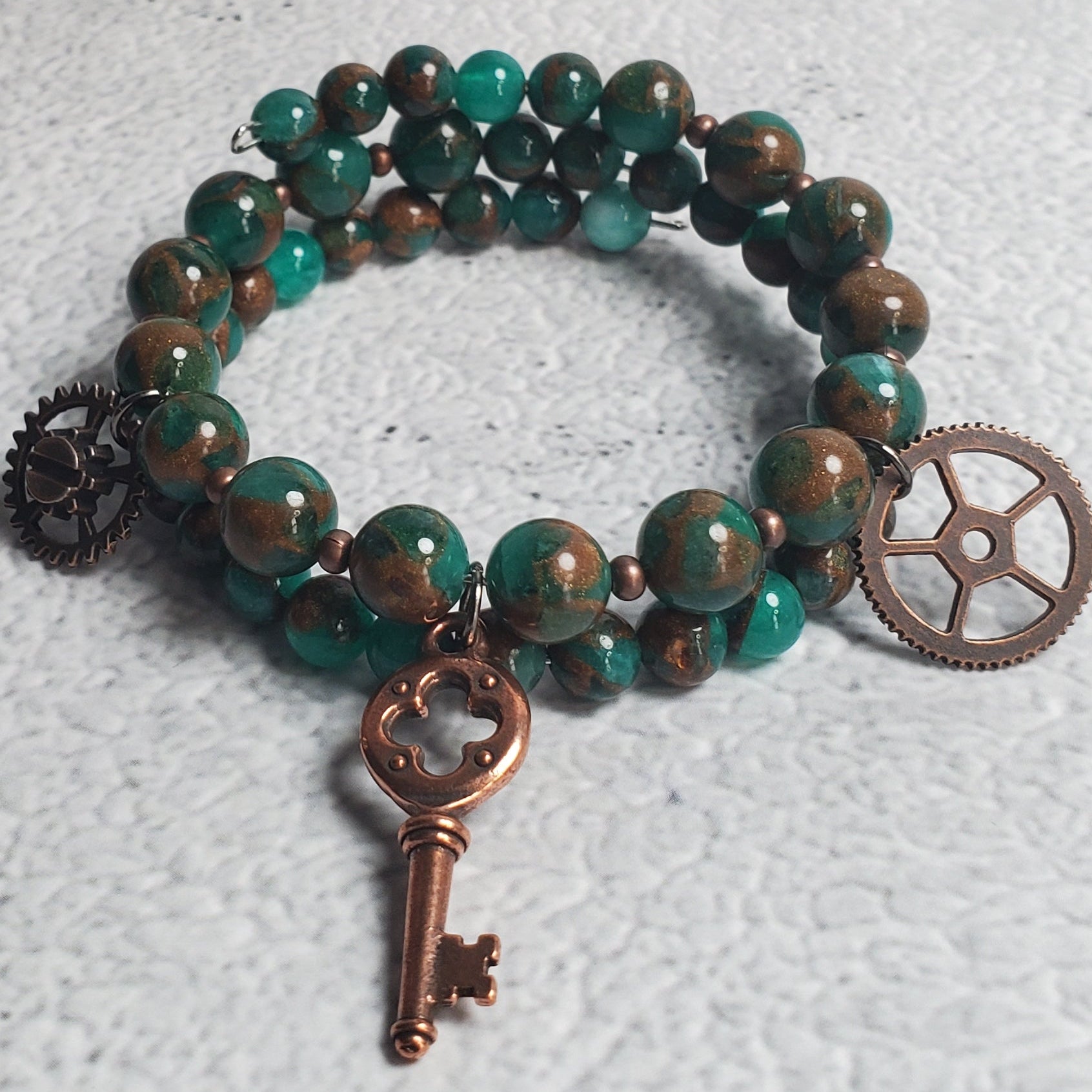 Handcrafted steampunk industrial bracelet with green resin sponge quartz, copper gear, and skeleton key charms on a memory wire cuff