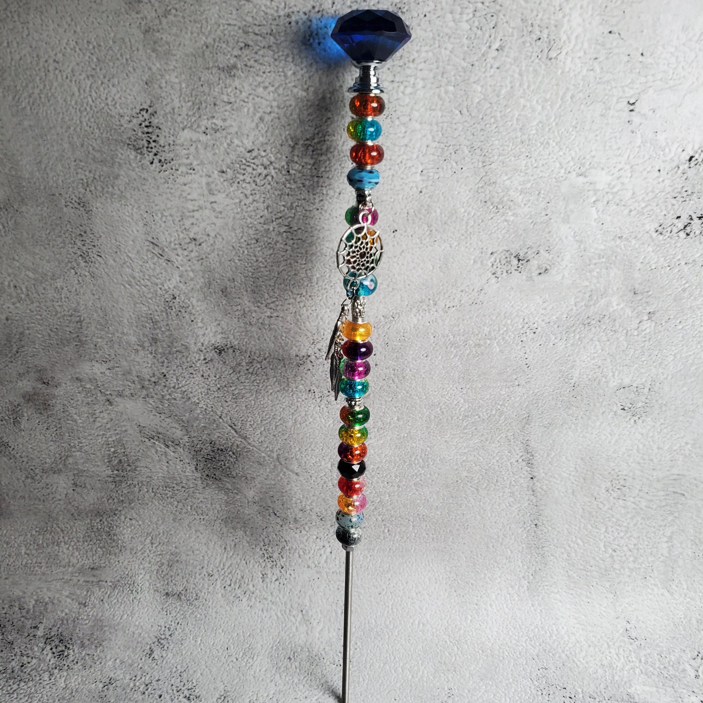 Decorative wand with colorful beads on a textured gray surface