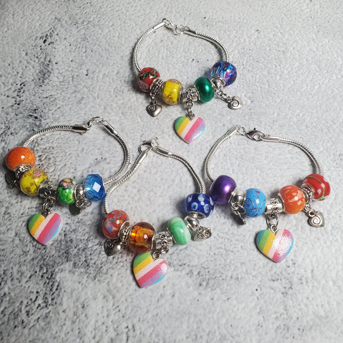 Colorful child’s charm bracelet with rainbow beads and heart charms on snake-chain base