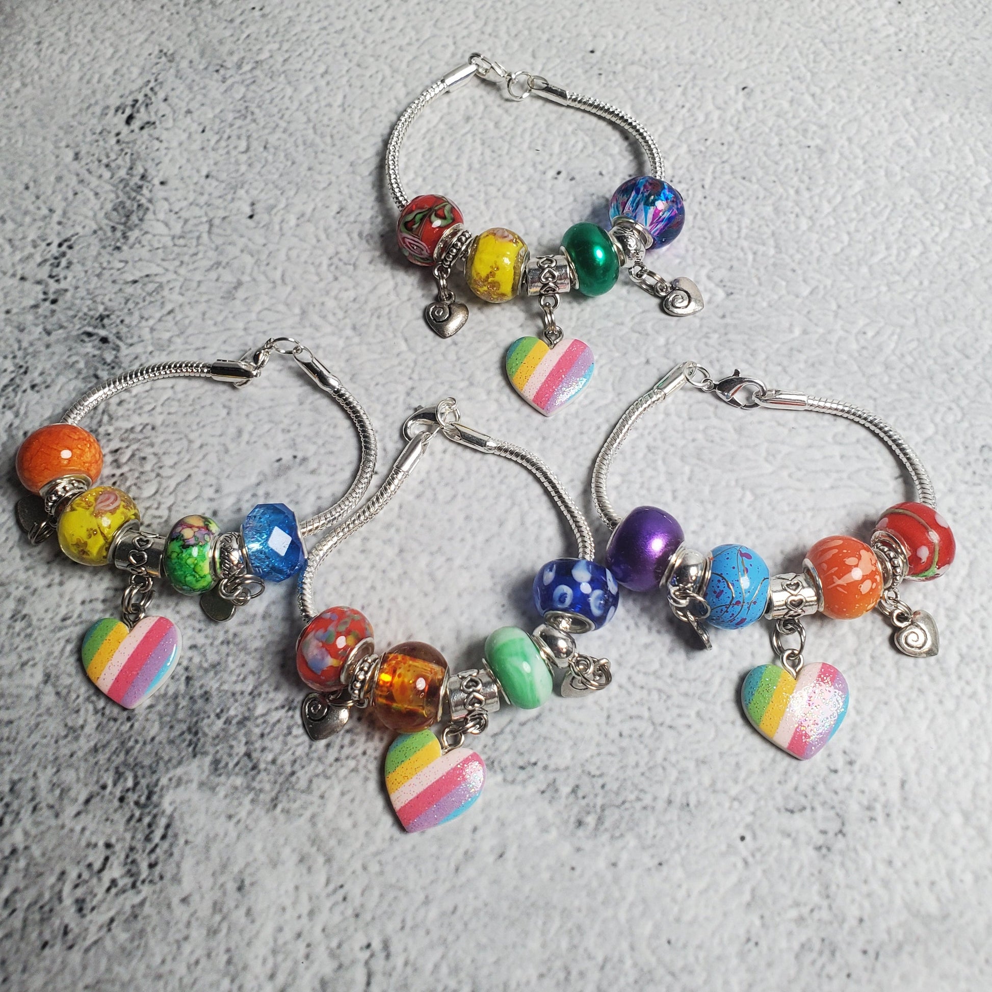 Colorful child’s charm bracelet with rainbow beads and heart charms on snake-chain base