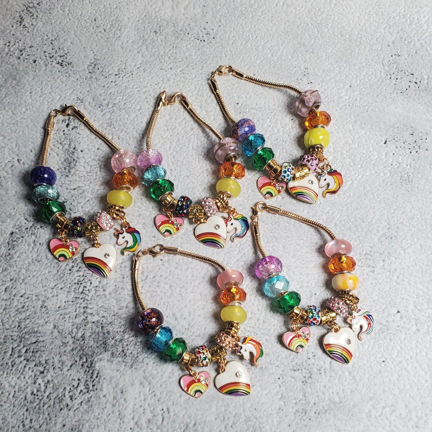 Colorful charm bracelet with rainbow beads and brass unicorn and heart charms on flexible snake chain