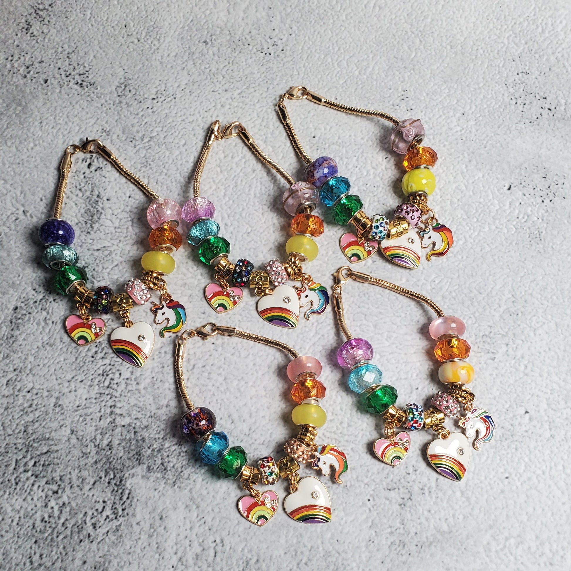 Colorful charm bracelet with rainbow beads and brass unicorn and heart charms on flexible snake chain