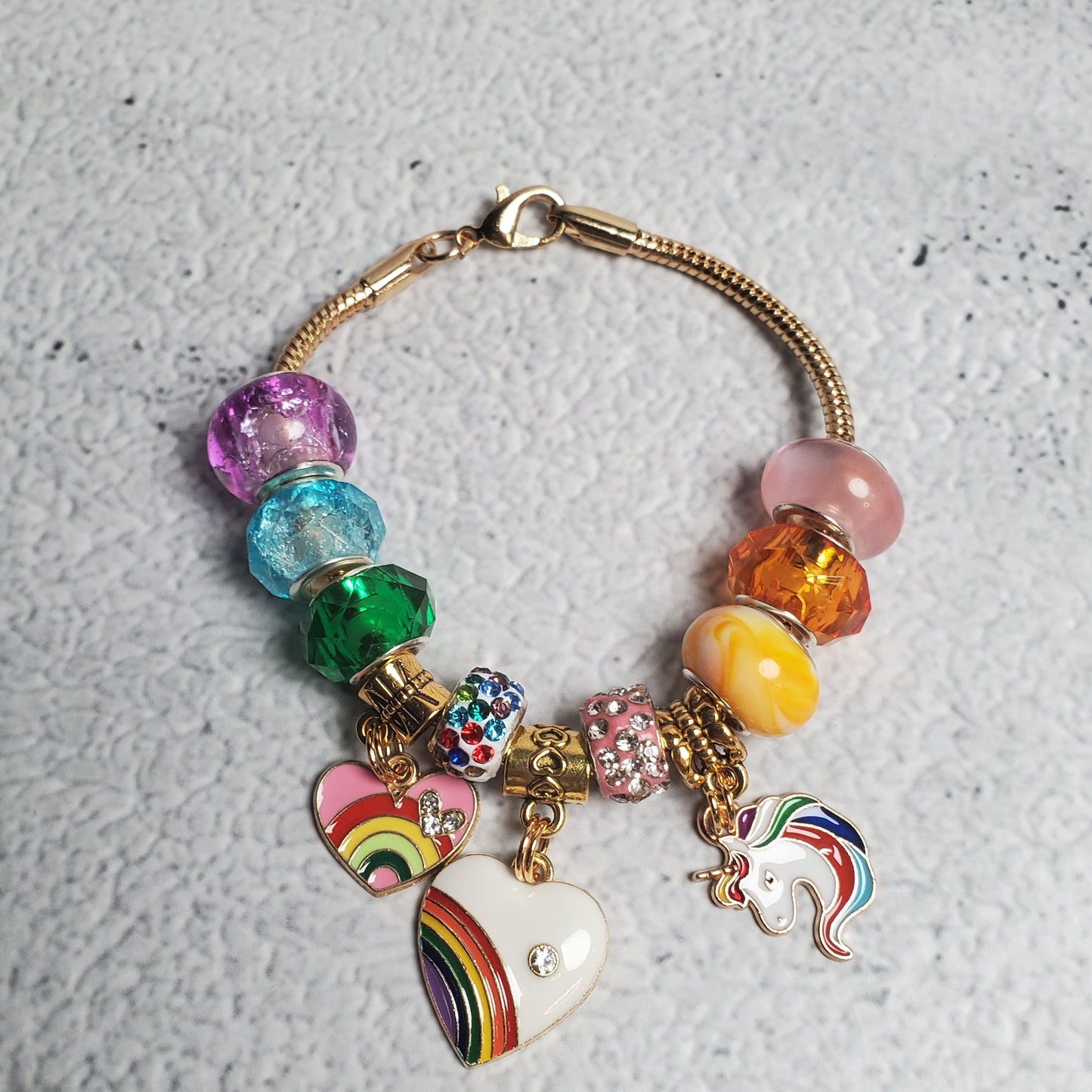 Colorful charm bracelet with rainbow beads and brass unicorn and heart charms on flexible snake chain