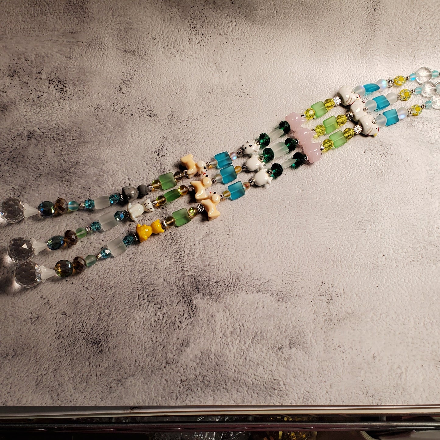 Handmade beaded suncatcher with dangling glass beads and a small glass animal beads, displayed on a textured gray paper sheet.