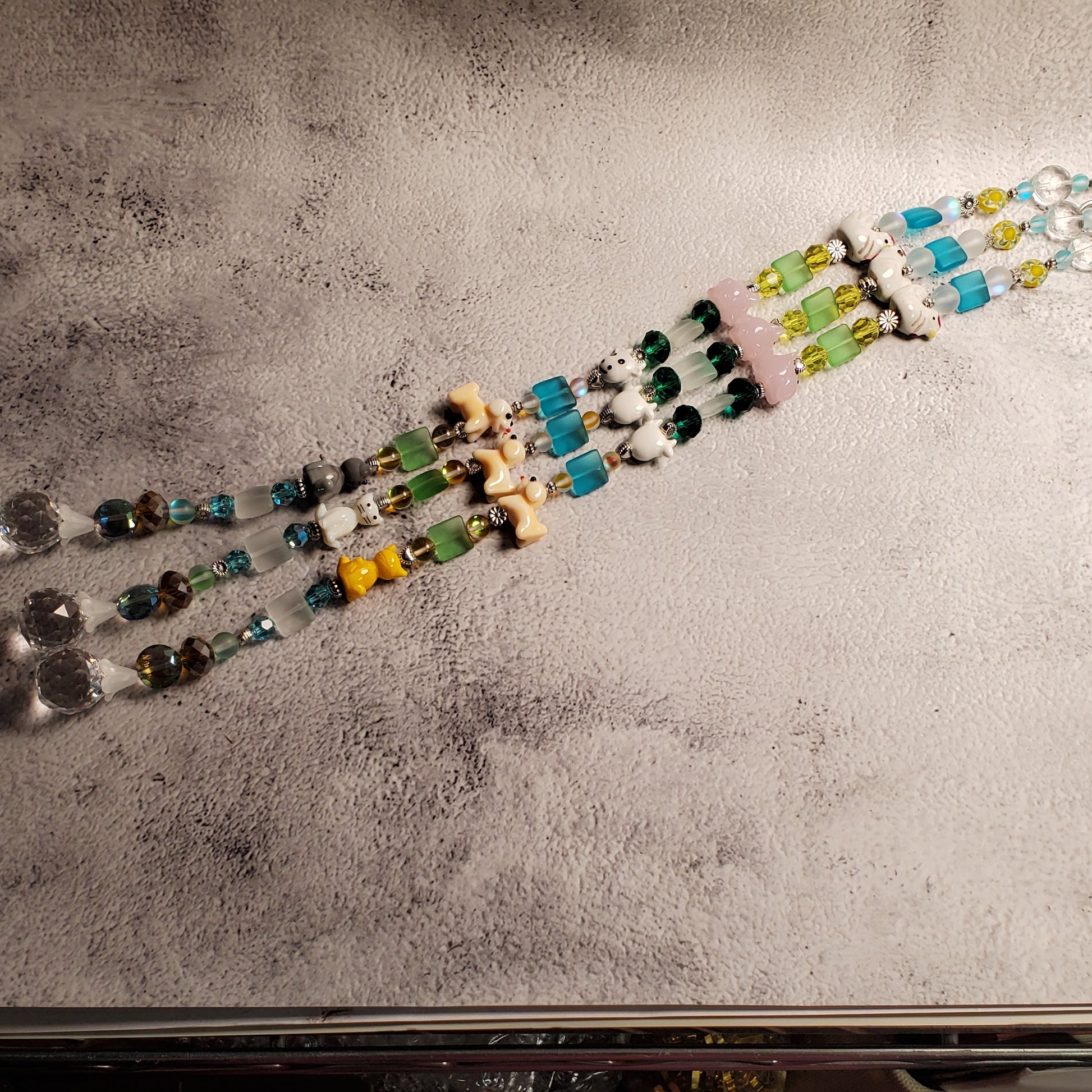 Handmade beaded suncatcher with dangling glass beads and a small glass animal beads, displayed on a textured gray paper sheet.