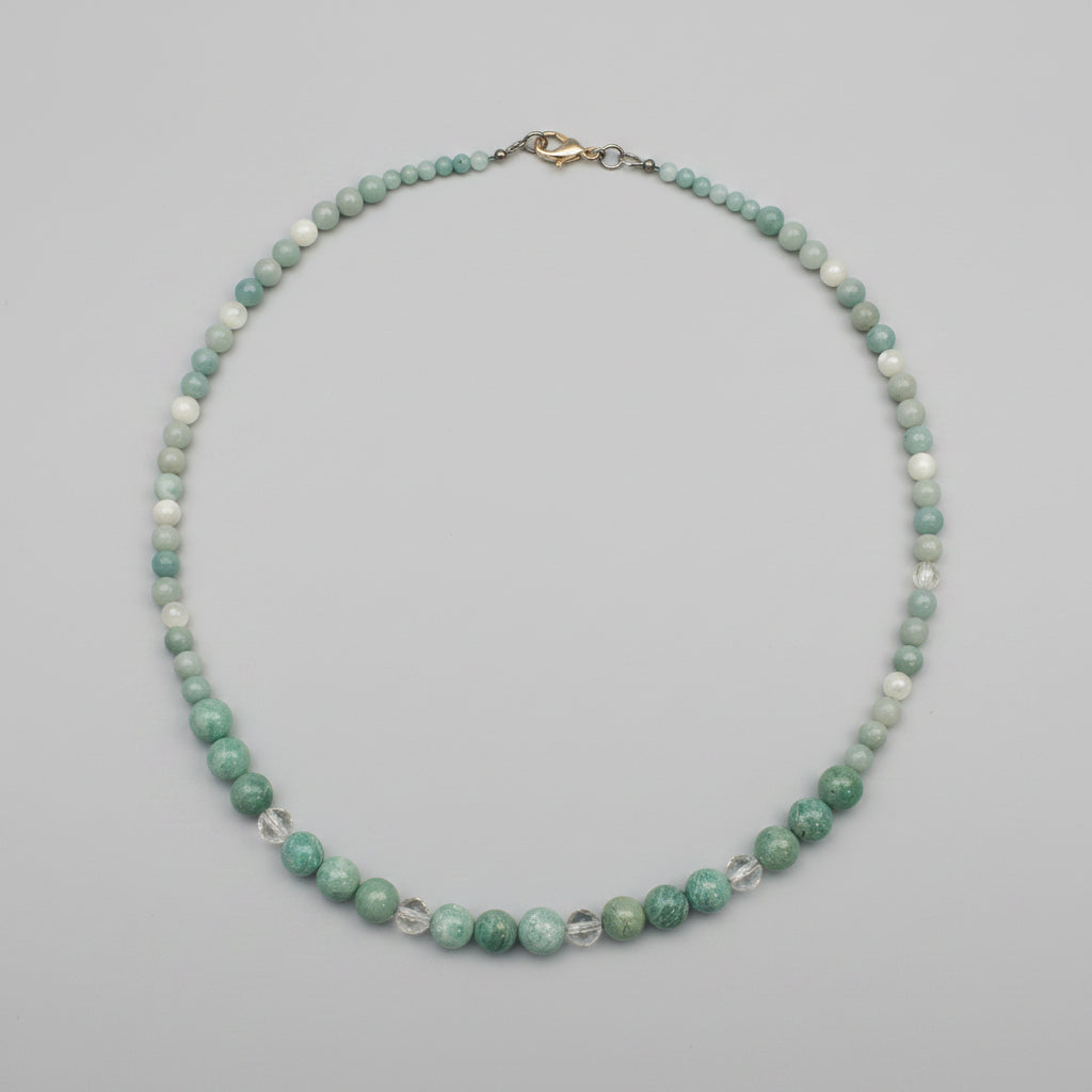 A beaded necklace made of small green and white marbled beads with a silver clasp, displayed on a textured gray surface.