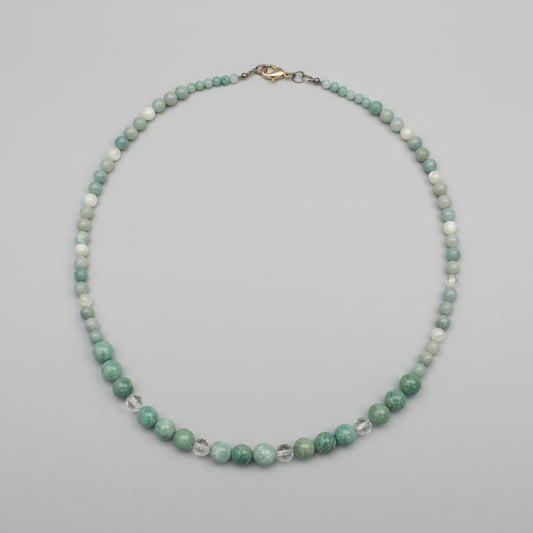 A beaded necklace made of small green and white marbled beads with a silver clasp, displayed on a textured gray surface.