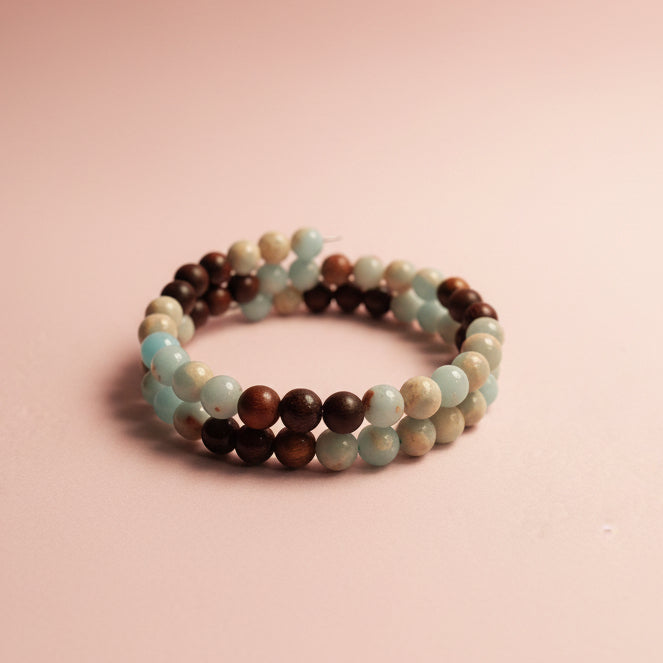 A beaded memory wire bracelet with alternating light blue, dark brown, and cream-colored round beads, displayed on a textured beige surface.