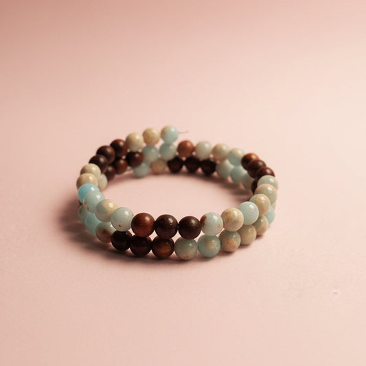A beaded memory wire bracelet with alternating light blue, dark brown, and cream-colored round beads, displayed on a textured beige surface.