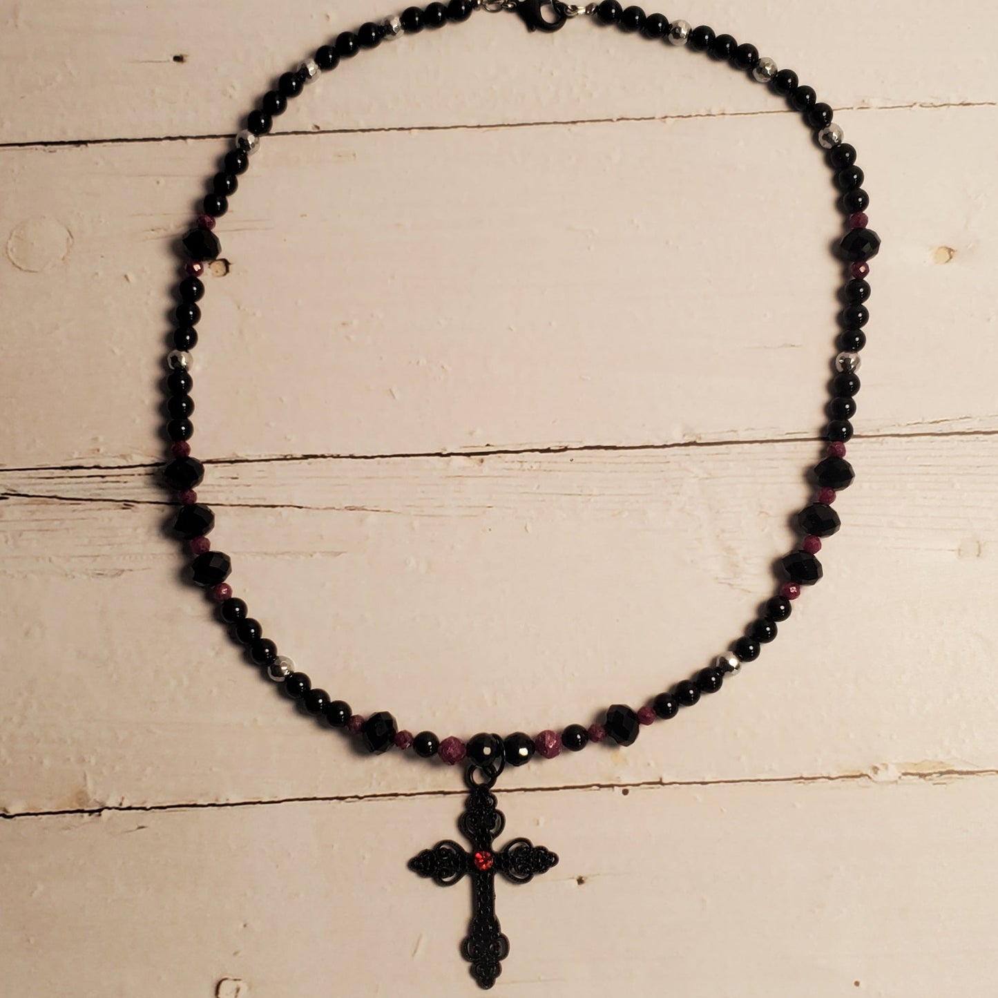 A black beaded necklace with a cross pendant resting on a white wooden surface.