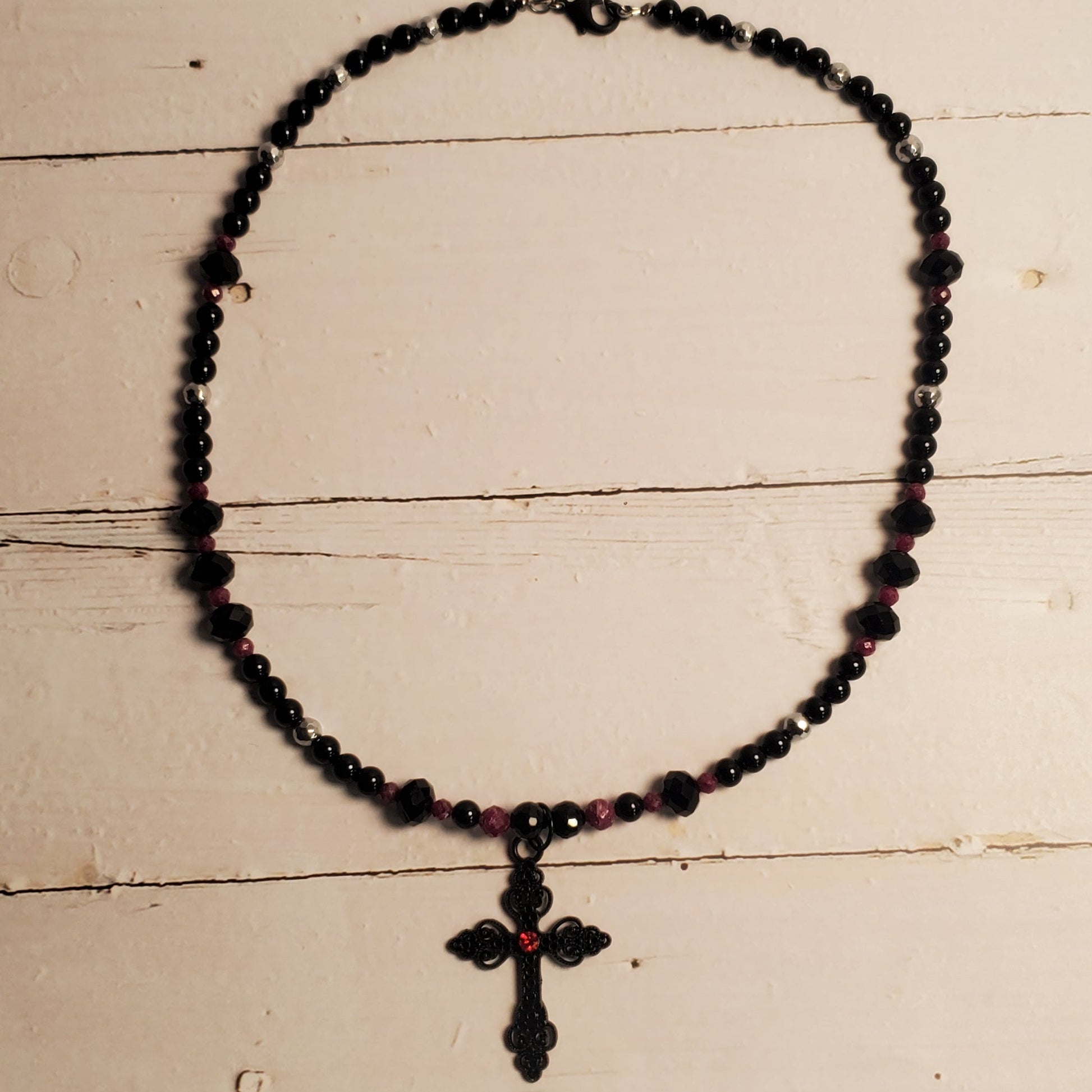 A black beaded necklace with a cross pendant resting on a white wooden surface.