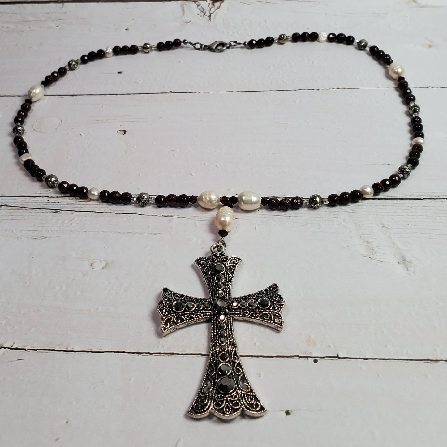 A beaded necklace with black and white beads and a silver filigree cross pendant, displayed on a white wooden surface.