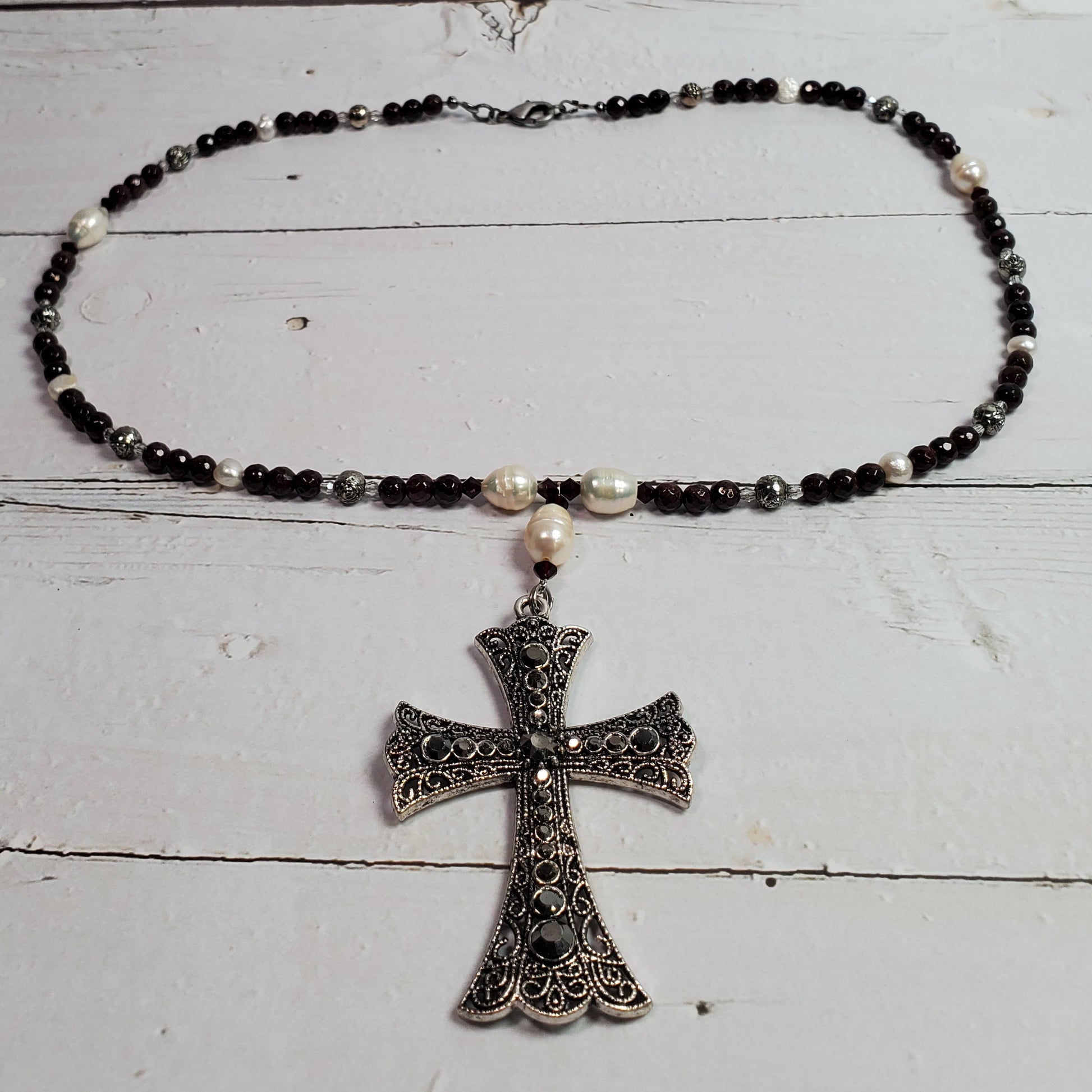 A beaded necklace with black and white beads and a silver filigree cross pendant, displayed on a white wooden surface.