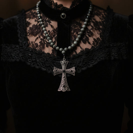A beaded rosary necklace with dark gray beads and a textured silver-toned cross pendant, laid flat on a white wooden surface.