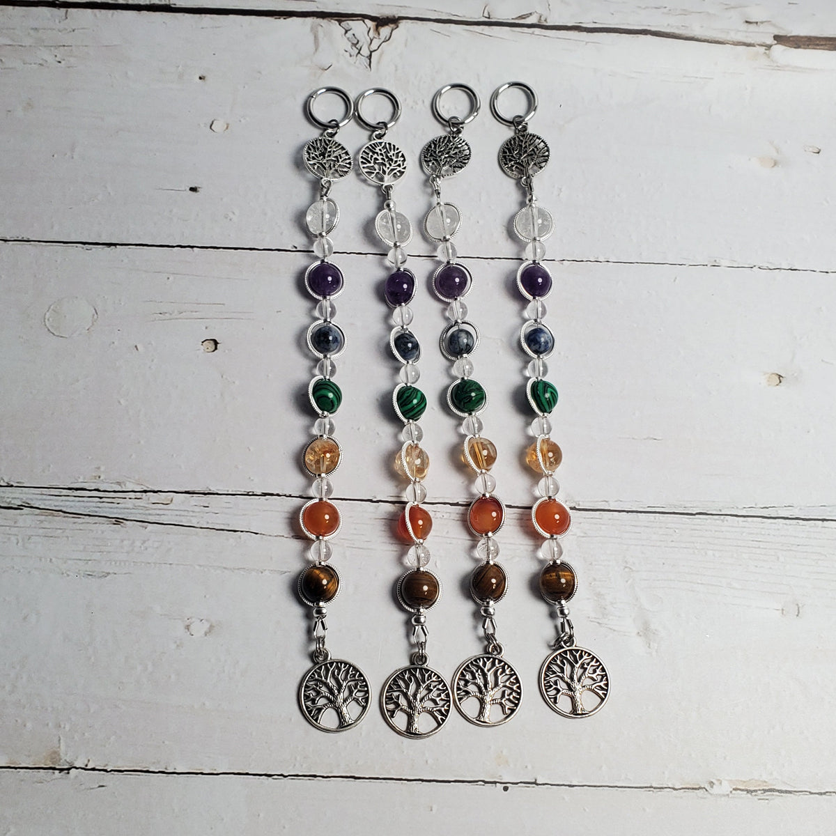Four beaded intention wall hangers with silver tree of life pendants, displayed on a white wooden background.