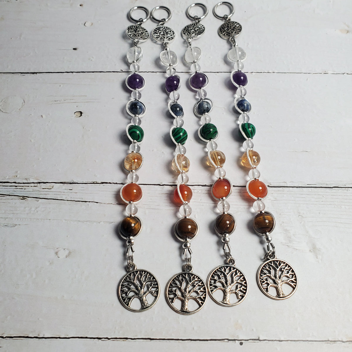 Four beaded intention wall hangers with silver tree of life charms, displayed on a white wooden background.