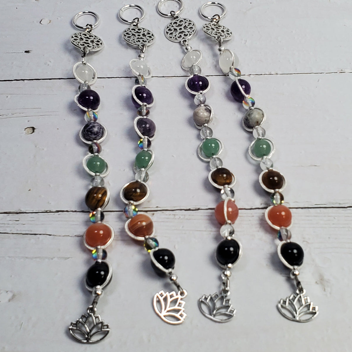 Four beaded wall hangers with silver-toned metal components, including a lotus flower charm, displayed on a white wooden plank background.