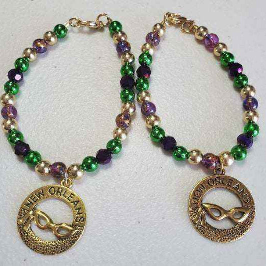 Mardi Gras charm bracelet with purple, green, and gold beads and brass mask charm, lobster clasp closure.